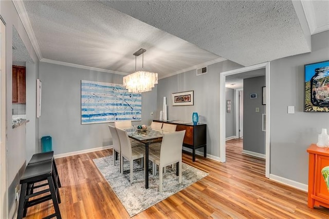 dining room featuring a textured ceiling, light wood-type flooring, crown molding, and a chandelier