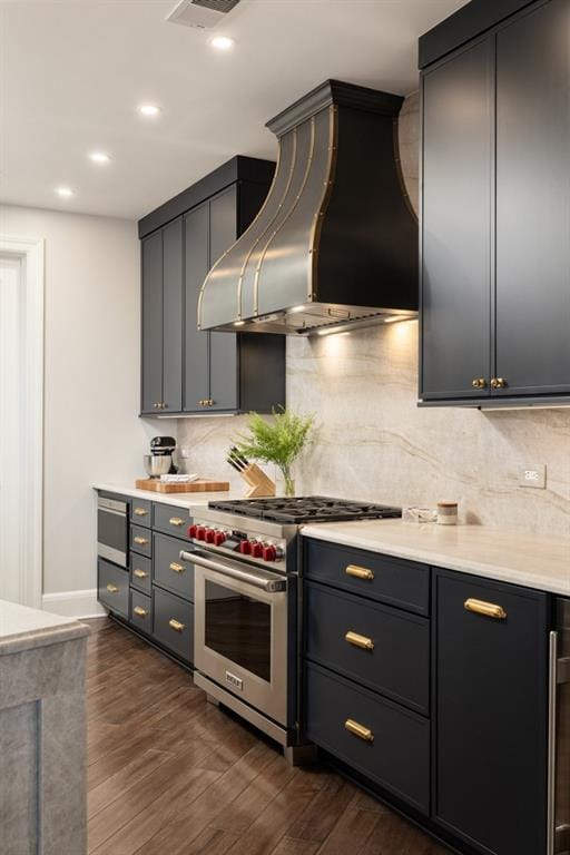 kitchen featuring wall chimney range hood, high end stove, decorative backsplash, and dark wood-type flooring