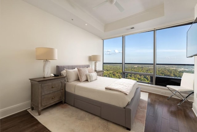 bedroom featuring a ceiling fan, baseboards, wood finished floors, a tray ceiling, and visible vents