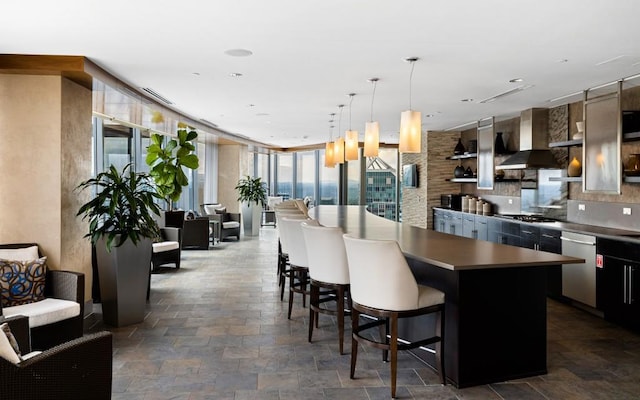 kitchen with wall chimney range hood, appliances with stainless steel finishes, stone tile flooring, and expansive windows