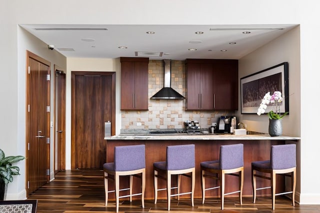 kitchen featuring decorative backsplash, a peninsula, a breakfast bar, dark wood-style floors, and wall chimney exhaust hood