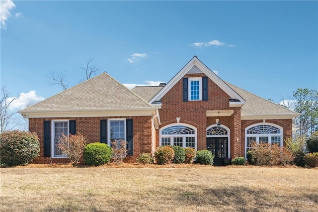 traditional-style home featuring a front lawn, roof with shingles, and brick siding