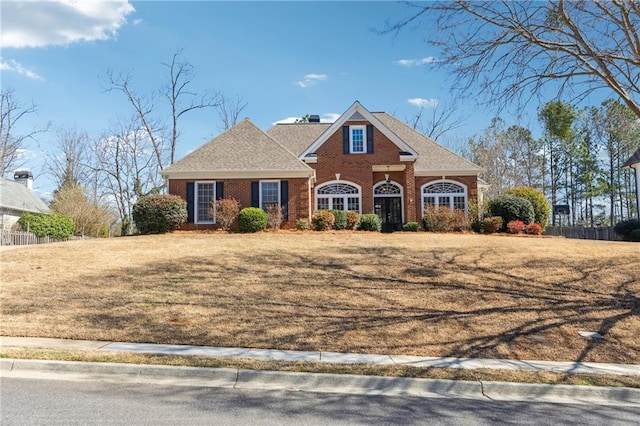 view of front of house featuring a shingled roof, a front yard, brick siding, and a chimney