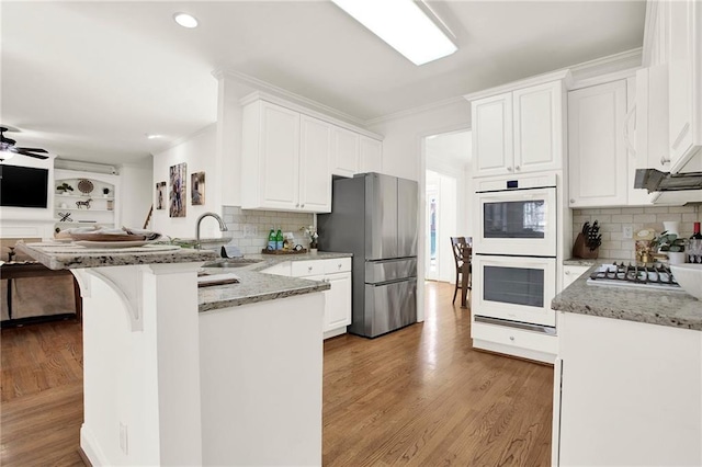 kitchen with appliances with stainless steel finishes, white cabinetry, light stone countertops, and kitchen peninsula