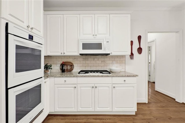 kitchen with white cabinetry, backsplash, white appliances, and light stone counters