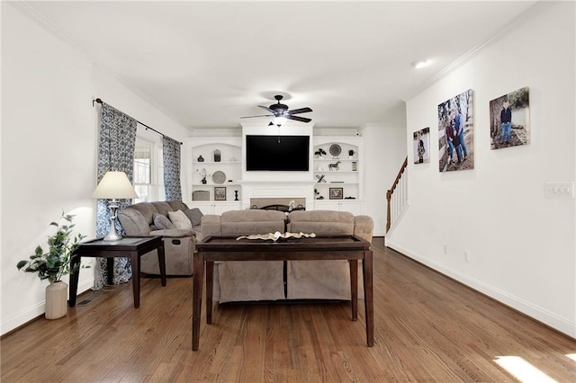 living room with built in shelves, crown molding, ceiling fan, and wood-type flooring