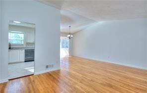 empty room featuring baseboards, lofted ceiling, an inviting chandelier, and wood finished floors