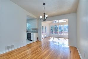 unfurnished living room featuring baseboards, wood finished floors, visible vents, and a chandelier