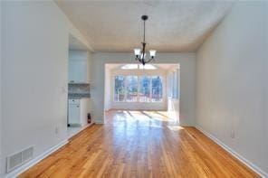 unfurnished dining area featuring a notable chandelier, wood finished floors, visible vents, and baseboards