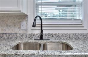 details featuring white cabinets, light stone countertops, and a sink