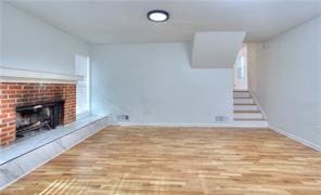 unfurnished living room featuring a brick fireplace, stairs, and wood finished floors