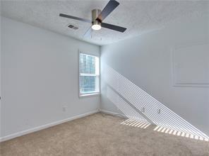 carpeted spare room with visible vents, baseboards, a textured ceiling, and a ceiling fan