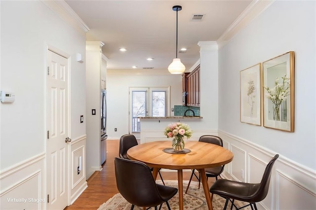 dining room with sink, wood-type flooring, and ornamental molding