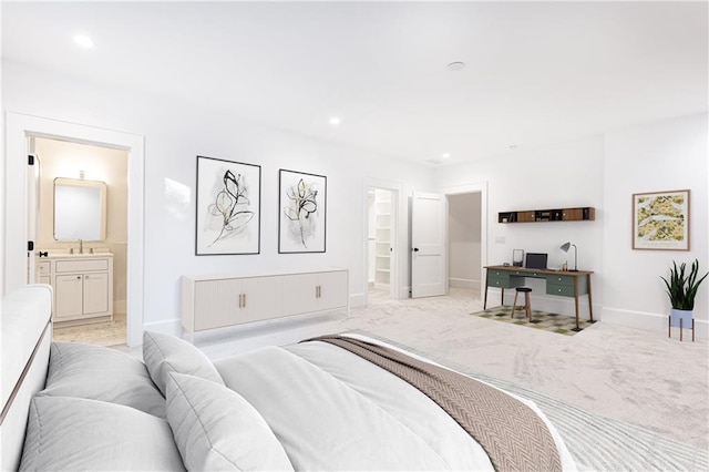 bedroom with ensuite bathroom, sink, a spacious closet, and light carpet