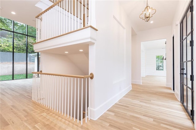 hall with light wood-type flooring, a towering ceiling, and a chandelier