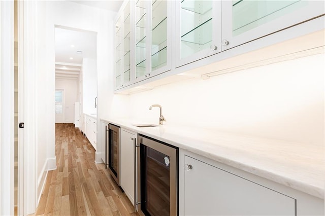 bar featuring white cabinets, light hardwood / wood-style flooring, beverage cooler, and sink