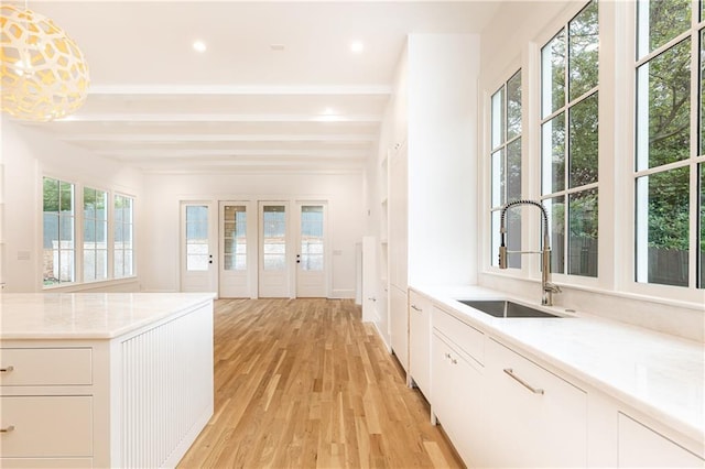 interior space with beam ceiling, sink, hanging light fixtures, light hardwood / wood-style flooring, and white cabinets