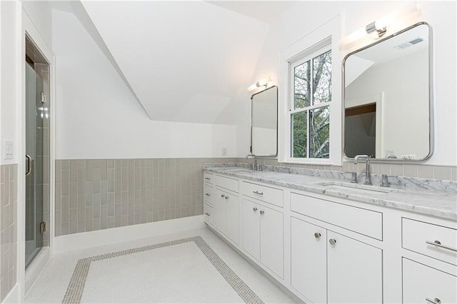 bathroom with tile patterned floors, vaulted ceiling, a shower with door, vanity, and tile walls