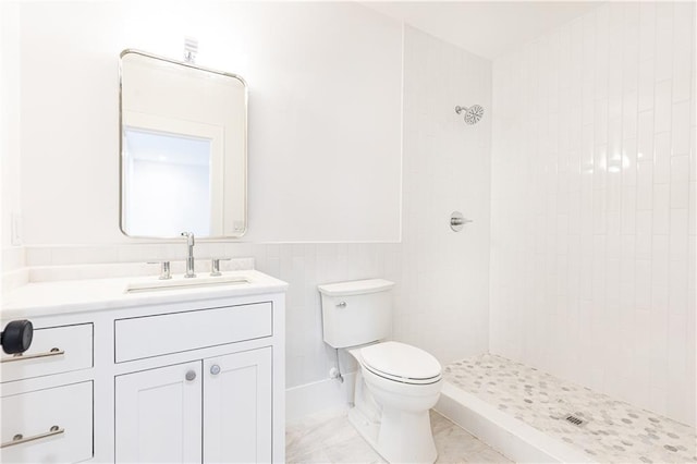 bathroom featuring a tile shower, vanity, and toilet