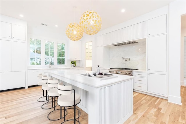 kitchen with a center island, light hardwood / wood-style flooring, backsplash, pendant lighting, and white cabinets