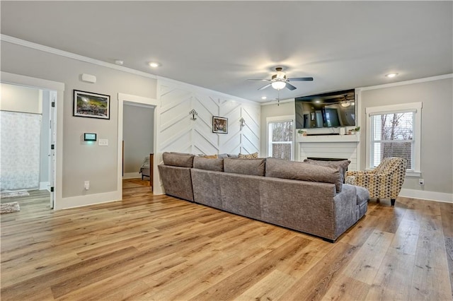 living room with ceiling fan, a large fireplace, crown molding, and light hardwood / wood-style flooring