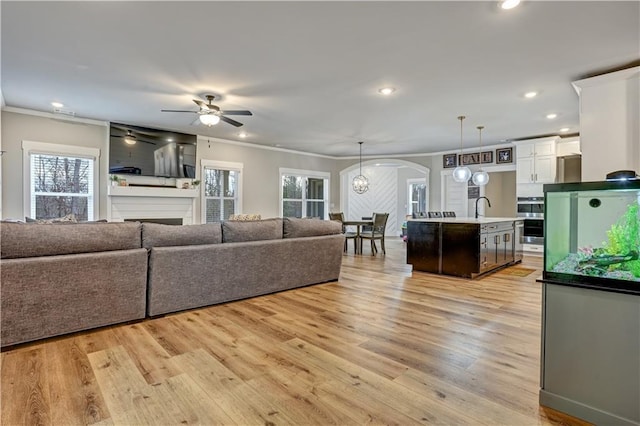 living room featuring ceiling fan with notable chandelier, sink, light hardwood / wood-style floors, and ornamental molding