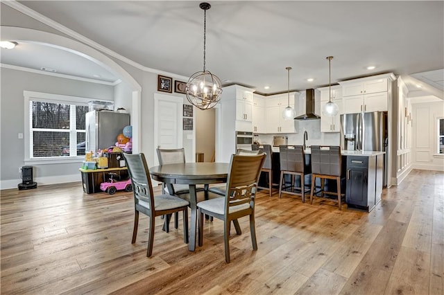 dining space featuring light wood-type flooring, ornamental molding, and an inviting chandelier