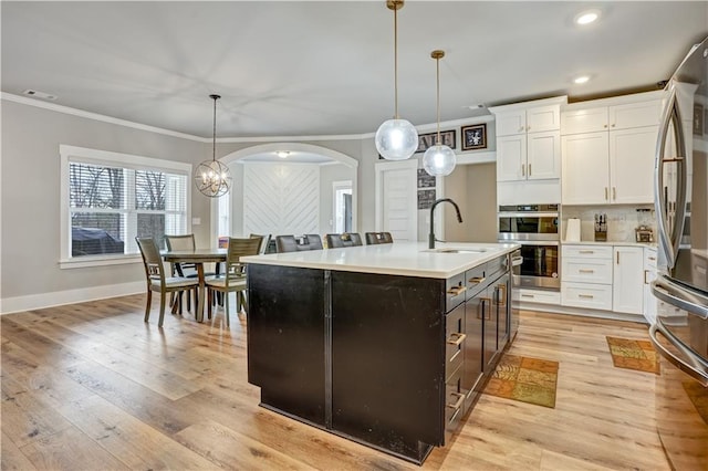 kitchen featuring decorative light fixtures, white cabinets, a kitchen island with sink, and sink