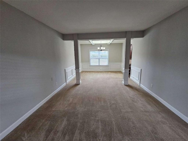 carpeted empty room featuring an inviting chandelier and ornate columns