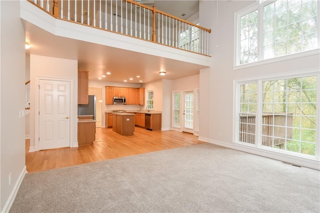 unfurnished living room with a towering ceiling, light hardwood / wood-style floors, and plenty of natural light