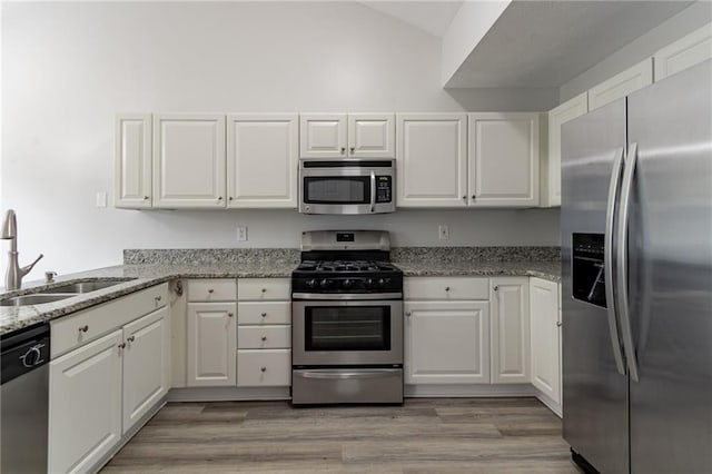 kitchen featuring appliances with stainless steel finishes, white cabinetry, light stone countertops, light hardwood / wood-style flooring, and sink