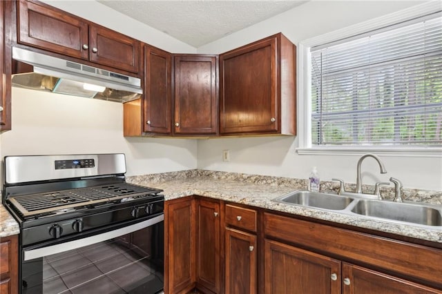 kitchen featuring a textured ceiling, stainless steel gas range, under cabinet range hood, and a sink