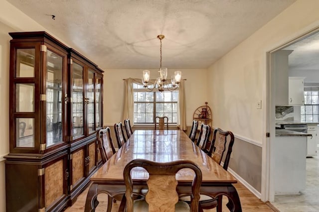 dining space featuring light wood finished floors, a chandelier, and a textured ceiling