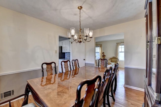 dining room with visible vents, a notable chandelier, baseboards, and wood finished floors