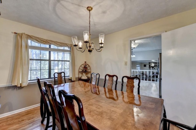 dining area with baseboards, wood finished floors, and ceiling fan with notable chandelier