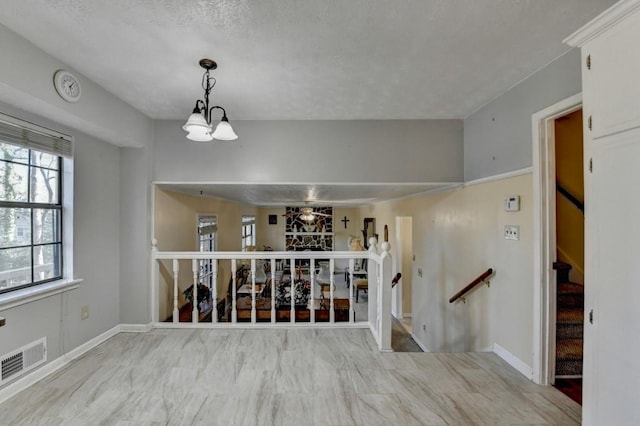 empty room with baseboards, a textured ceiling, visible vents, and a notable chandelier