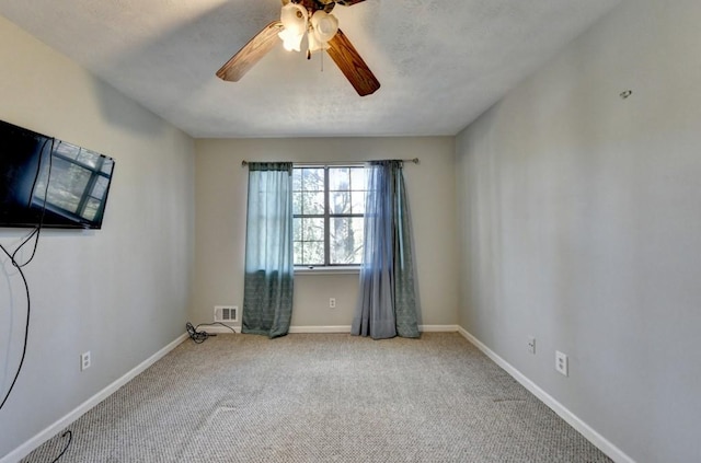 unfurnished room featuring carpet floors, visible vents, baseboards, and a ceiling fan