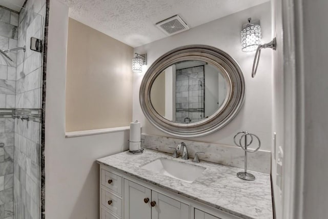 bathroom with a tile shower, a textured ceiling, vanity, and visible vents