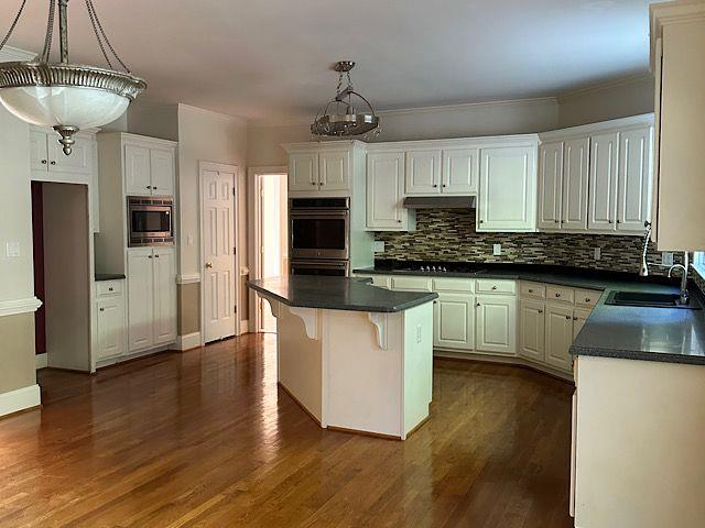 kitchen with appliances with stainless steel finishes, dark hardwood / wood-style flooring, white cabinets, and a kitchen island