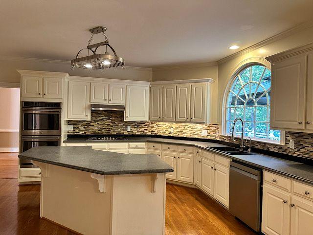 kitchen with a kitchen bar, white cabinets, wood-type flooring, and appliances with stainless steel finishes