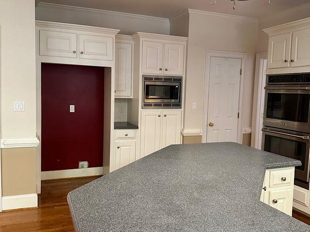 kitchen featuring white cabinetry, ornamental molding, dark wood-type flooring, and appliances with stainless steel finishes