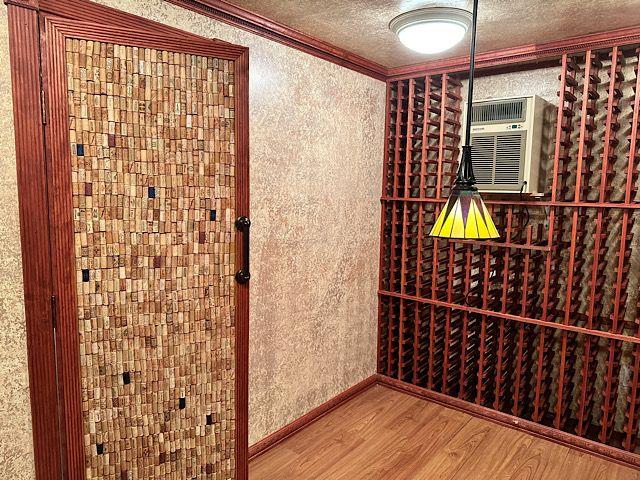 wine room with a textured ceiling, hardwood / wood-style flooring, a wall unit AC, and crown molding