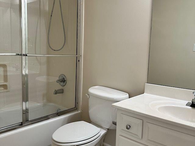 full bathroom featuring vanity, bath / shower combo with glass door, and toilet