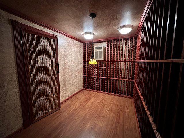 wine cellar featuring hardwood / wood-style flooring, a wall mounted AC, and ornamental molding