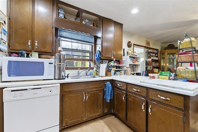 kitchen with a sink, a peninsula, white appliances, light wood-style flooring, and light countertops