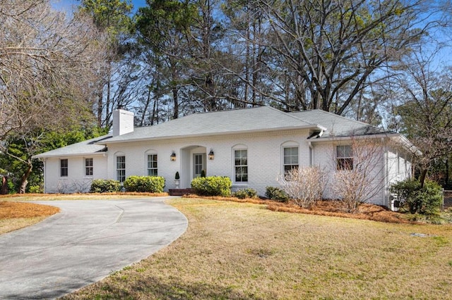 single story home featuring a front yard, brick siding, driveway, and a chimney