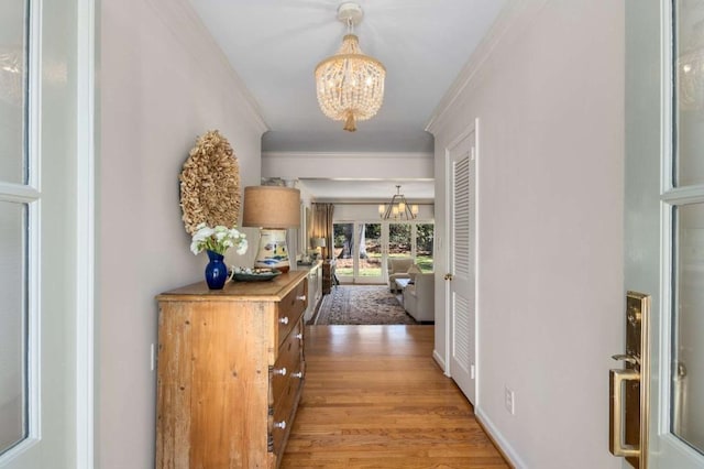 corridor featuring crown molding, light wood-type flooring, baseboards, and an inviting chandelier