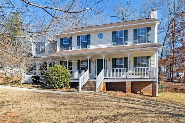 colonial inspired home with a porch, a front yard, and a chimney