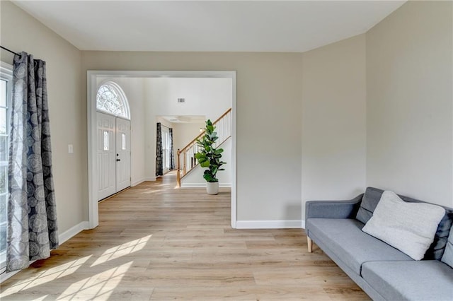 foyer entrance with light wood-style flooring, stairs, and baseboards