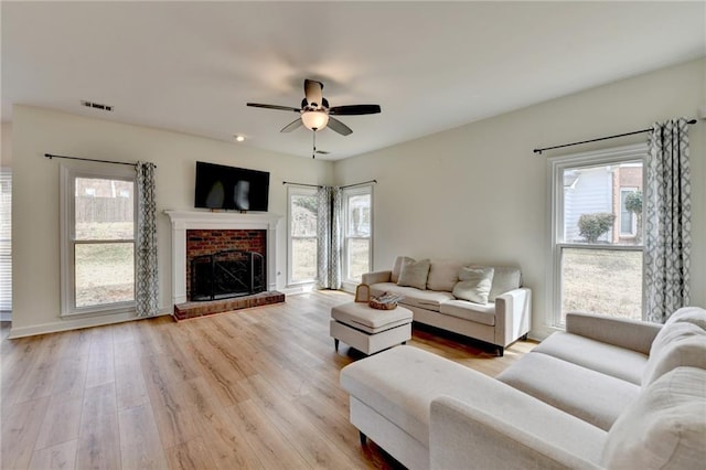 living room with a brick fireplace, light wood-style flooring, visible vents, and ceiling fan